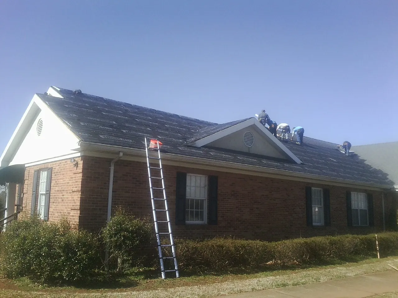 Crew tearing shingles off a brick ranch roof with a ladder set — Metal Roof Repair work by our crew in Fremont